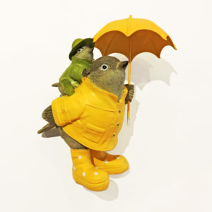 Ceramic figurine of a dove with a yellow umbrella, wearing a greyish brown raincoat, and carrying a smaller dove on its back.